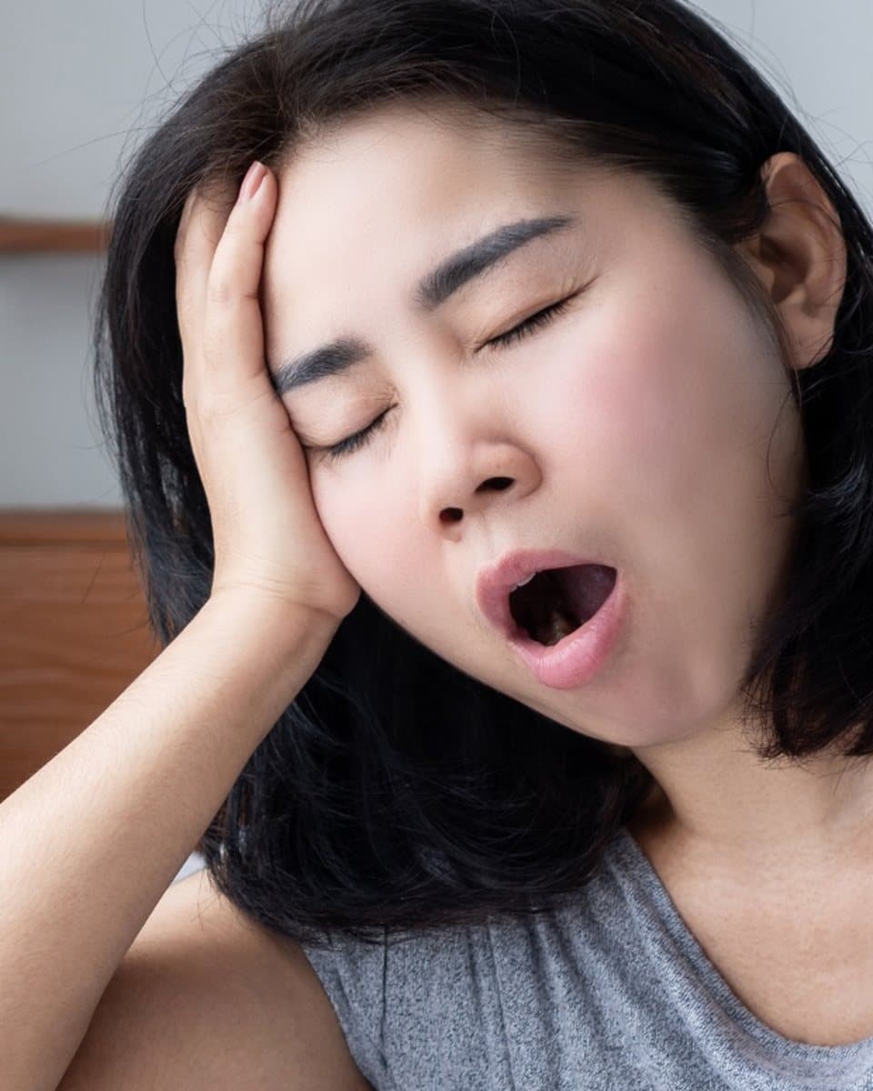 Femme qui baille au réveil, assise dans son lit, encore fatiguée