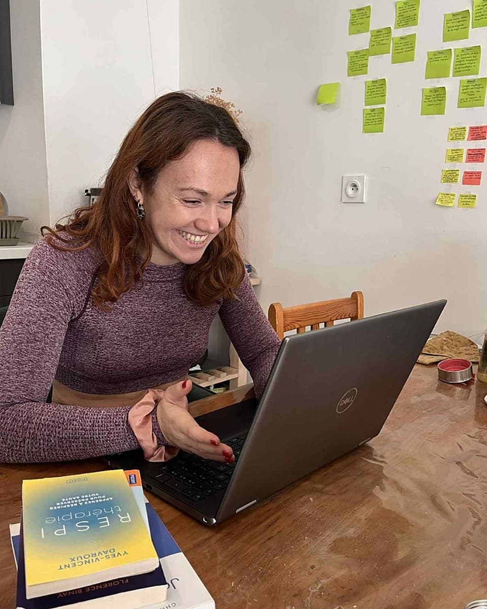 Amélie Monkarey souriante devant son ordinateur pendant une séance de sophrologie en visio